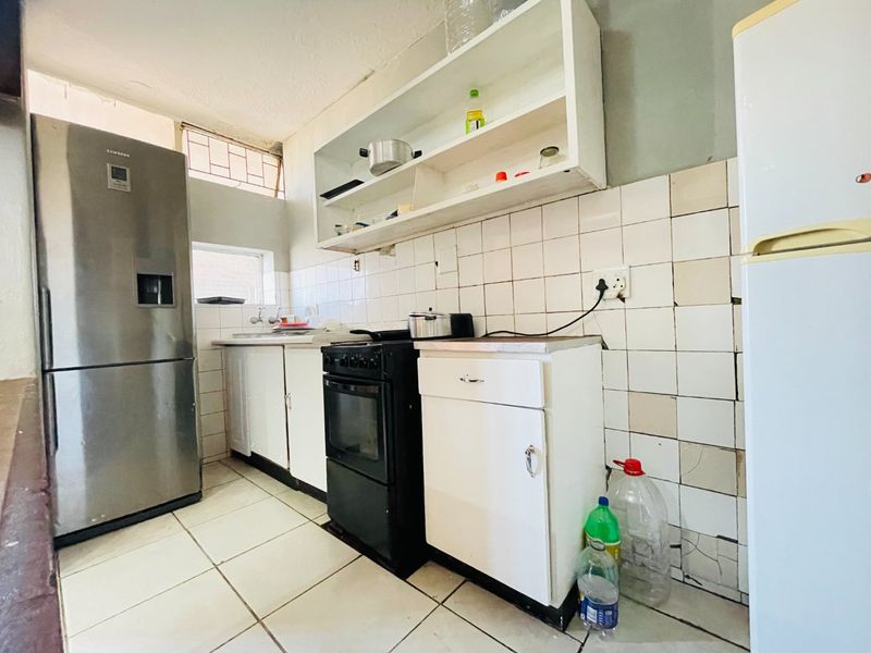 A functional kitchen featuring tiled splashbacks, built-in cabinetry, and a freestanding stove, currently showing signs of wear and requiring cosmetic updates.