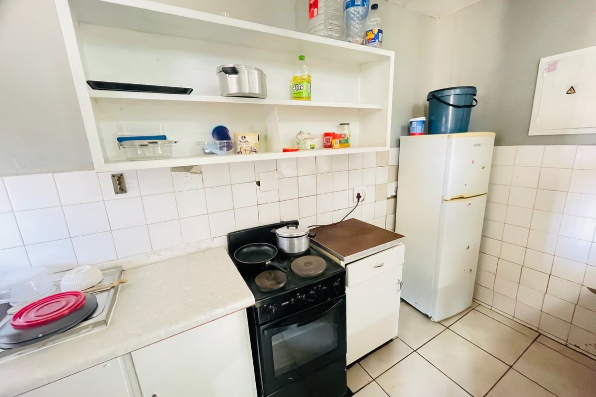 A compact kitchen featuring tiled walls, laminate countertops, built-in shelving, and an electric stove, requiring cosmetic updates to improve its overall condition.