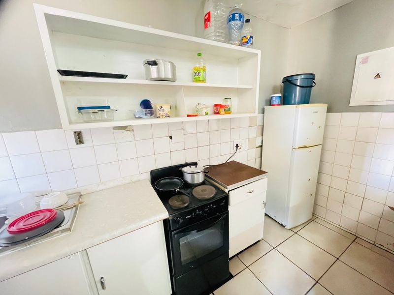 A compact kitchen featuring tiled walls, laminate countertops, built-in shelving, and an electric stove, requiring cosmetic updates to improve its overall condition.