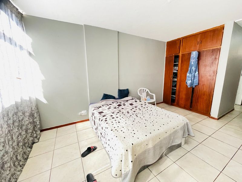A bedroom featuring tiled flooring and a large built-in wooden wardrobe, offering functional storage space with potential for cosmetic updates.