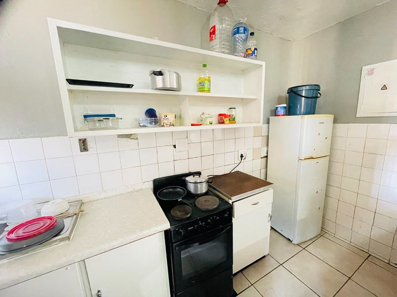 A compact kitchen featuring built-in shelving, ceramic wall tiling, and an electric stove, requiring some maintenance and cosmetic updates.