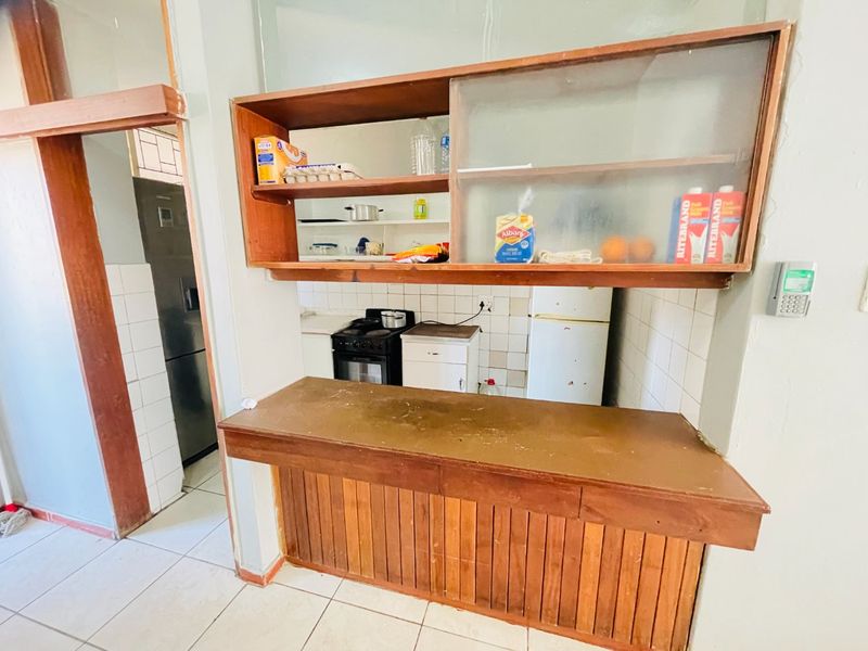 A dated kitchen featuring wooden cabinetry, a breakfast counter, and tiled splashbacks, offering potential for a modern renovation.