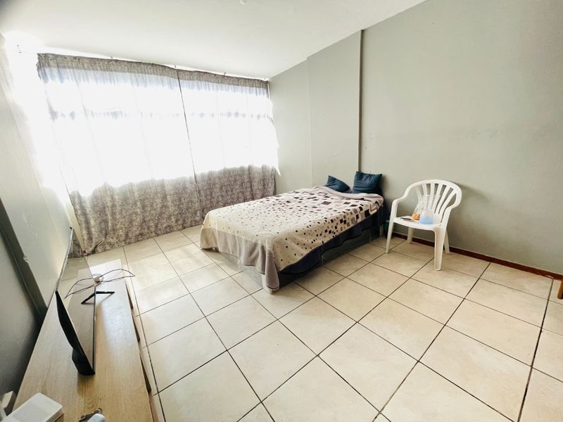 A bedroom featuring tiled flooring and a large window with curtains, providing natural light. The space requires cosmetic updates to the wall finishes.