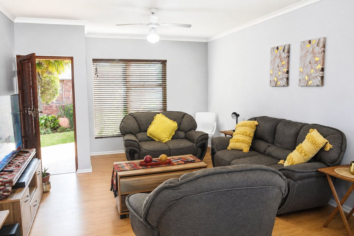 A well-maintained living room featuring laminate flooring, a ceiling fan, and direct access to the garden through a side door.