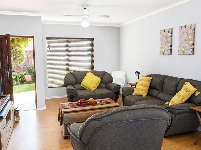 A well-maintained living room featuring laminate flooring, a ceiling fan, and direct access to the garden through a side door.