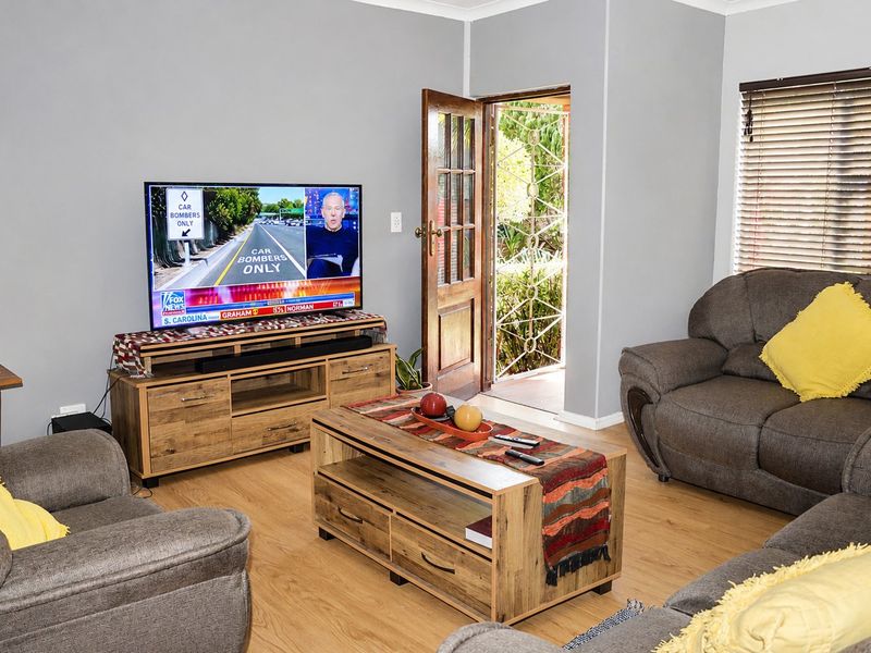 A comfortable living room featuring laminate flooring, coving, and a timber-framed glass door providing direct access to the outdoor area.