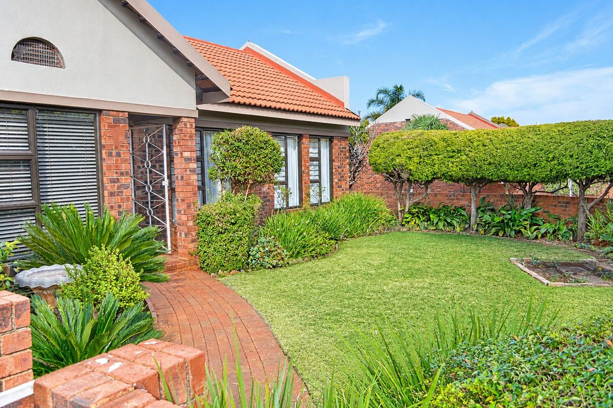 A well-maintained rear garden area featuring a brick paved pathway, established landscaping, and a classic brick townhouse facade with terracotta roof tiles.