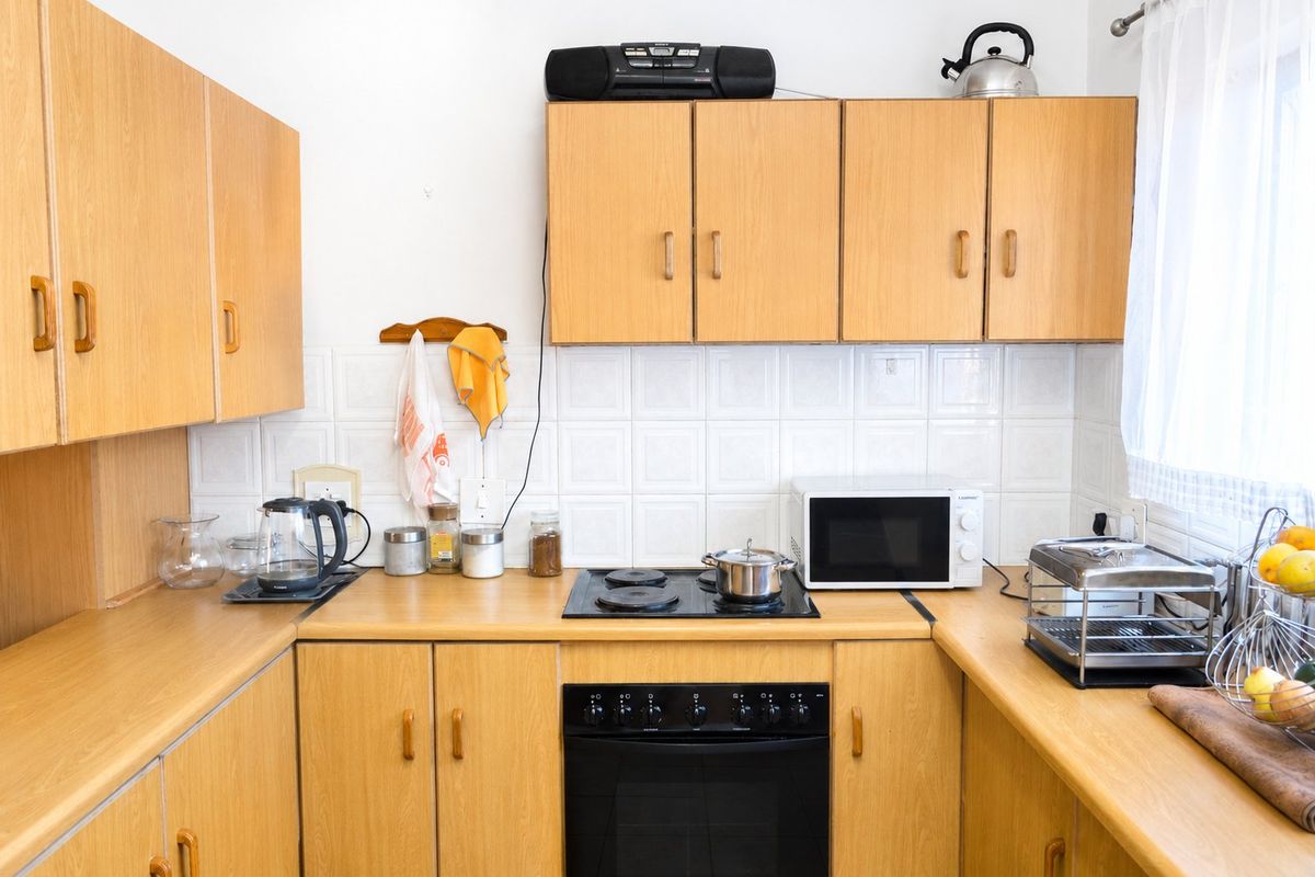 A functional kitchen featuring light wood-look laminate cabinetry, matching countertops, a ceramic tile backsplash, and a built-in electric oven with a hob.
