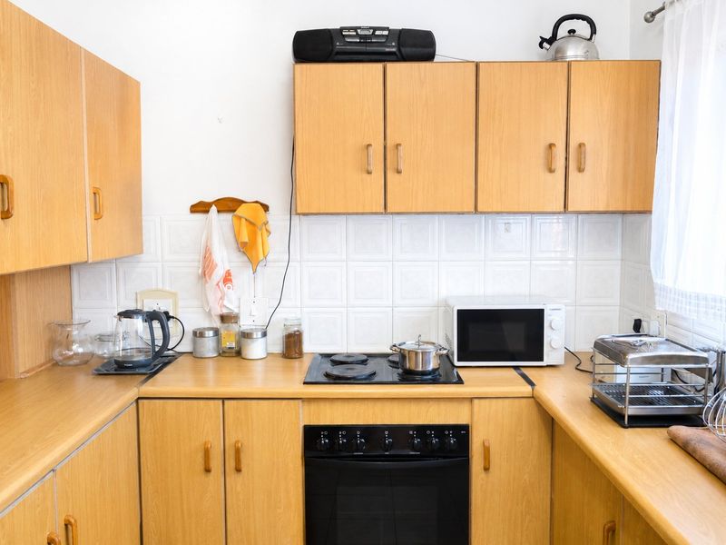 A functional kitchen featuring light wood-look laminate cabinetry, matching countertops, a ceramic tile backsplash, and a built-in electric oven with a hob.