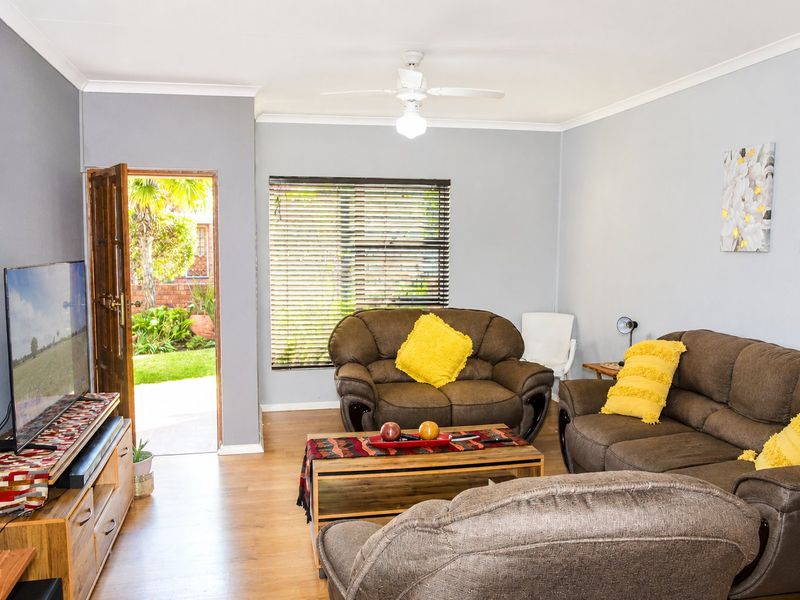 A comfortable living room featuring laminate flooring, a ceiling fan, and direct access to the garden through a timber door.
