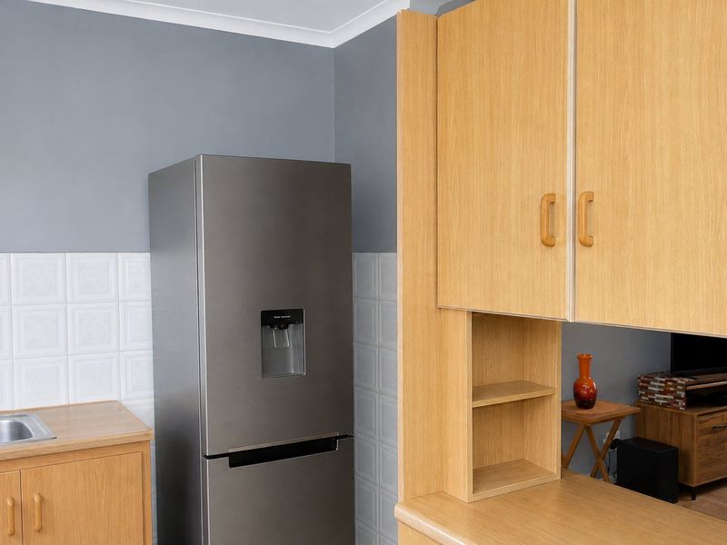 A functional kitchen area featuring light wood cabinetry, a tiled backsplash, and a stainless steel sink, with a view into the adjacent living space.