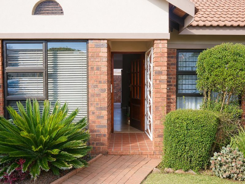 Front entrance of a townhouse featuring a face brick facade, tiled roof, security gate, and a paved walkway leading to the timber front door.