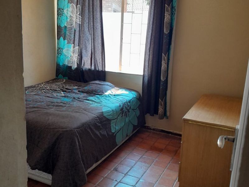 A bedroom featuring terracotta tiled flooring, a ceiling fan, and security bars on the window, requiring cosmetic updates to improve its overall condition.