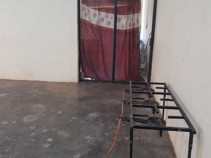 An unfinished kitchen area featuring concrete flooring, a sliding glass door, and a basic gas burner stand, requiring significant renovation and finishing.