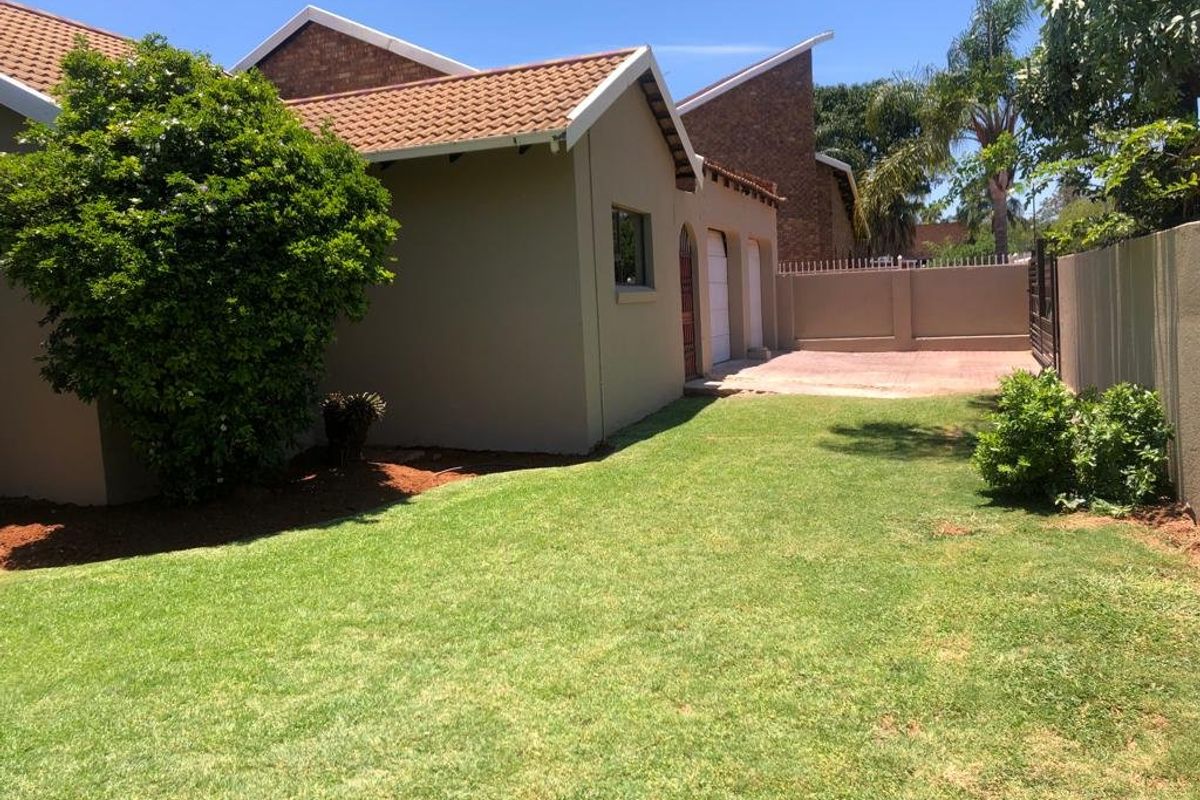 A view of the rear exterior of the house featuring a well-maintained lawn, paved driveway, and boundary wall.