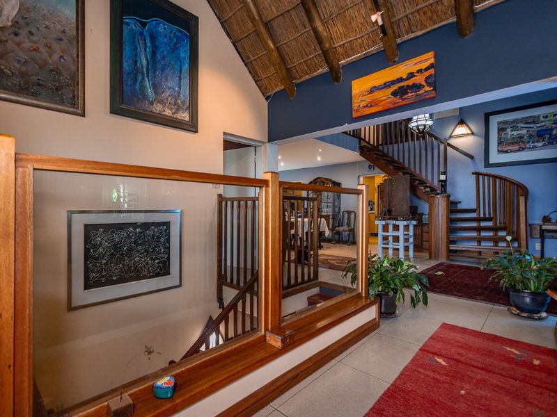Spacious hallway featuring a timber staircase with glass balustrade and a distinctive exposed thatched roof ceiling, connecting multiple living areas.