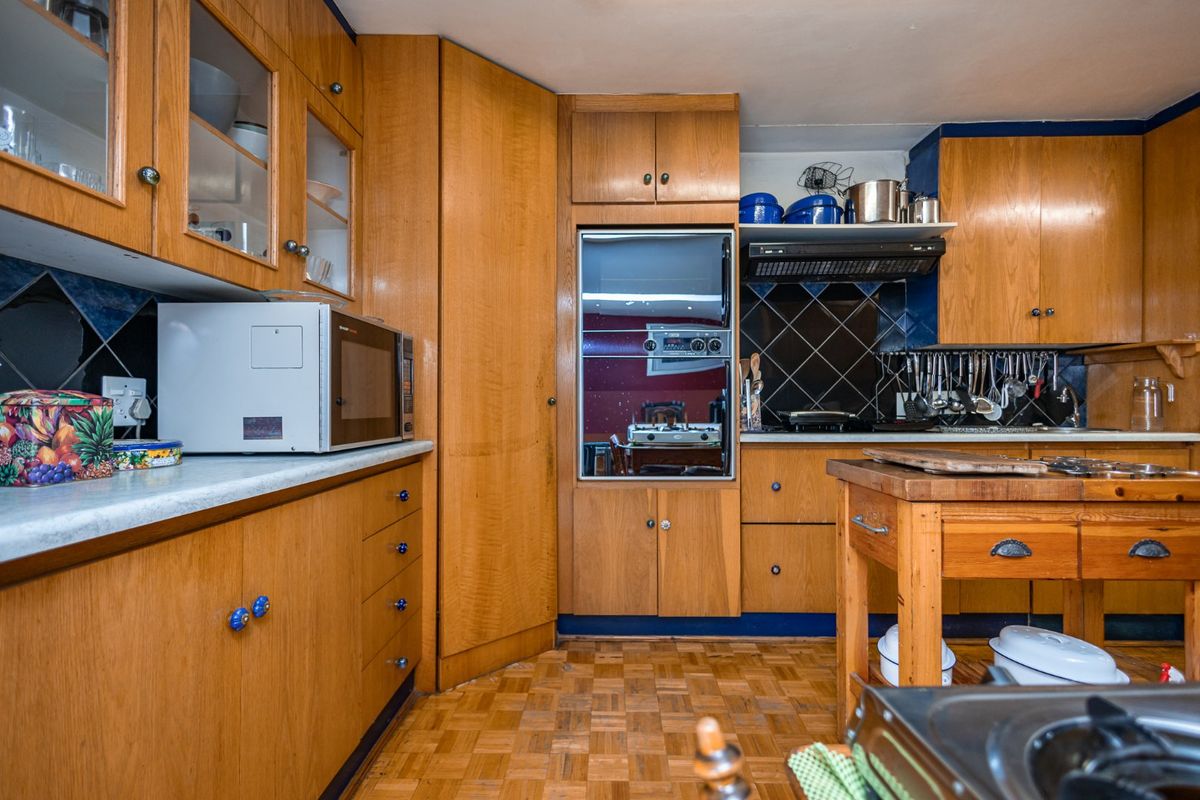 A traditional kitchen featuring extensive wooden cabinetry, integrated oven, extractor fan, and classic parquet flooring with a tiled backsplash.