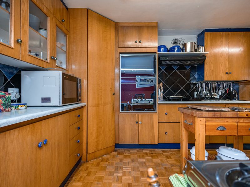 A traditional kitchen featuring extensive wooden cabinetry, integrated oven, extractor fan, and classic parquet flooring with a tiled backsplash.