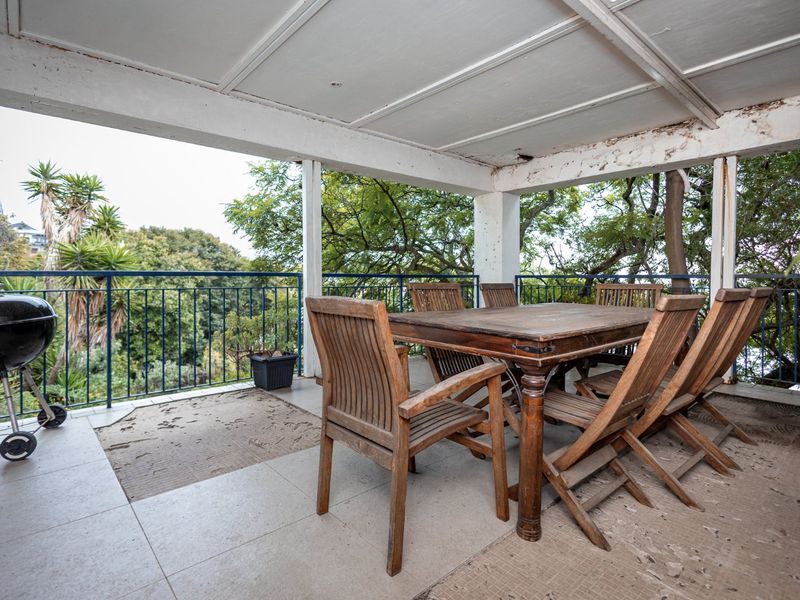 Covered outdoor patio area featuring tiled flooring and a metal balustrade, offering a functional space for outdoor dining with views of the surrounding trees.