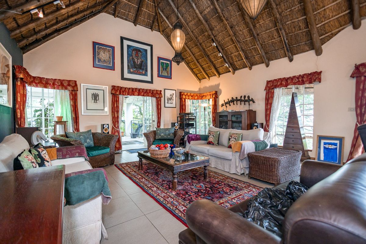 Spacious living room featuring a high vaulted thatched ceiling with exposed timber rafters, tiled flooring, and direct access to an outdoor patio area.