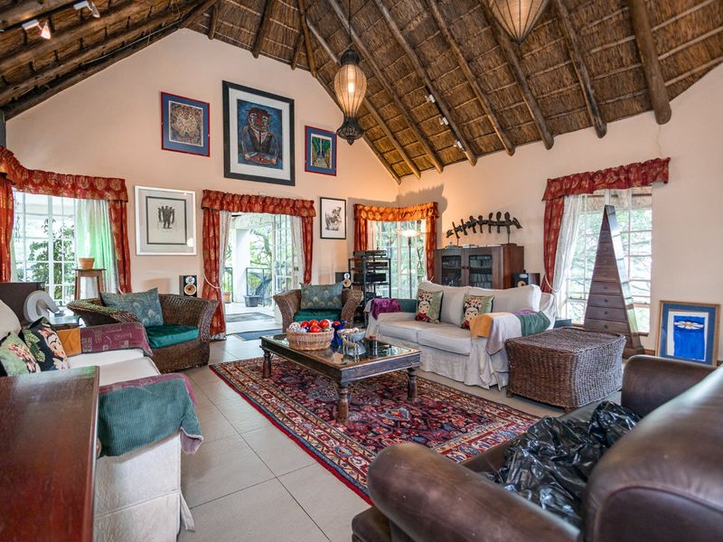 Spacious living room featuring a high vaulted thatched ceiling with exposed timber rafters, tiled flooring, and direct access to an outdoor patio area.