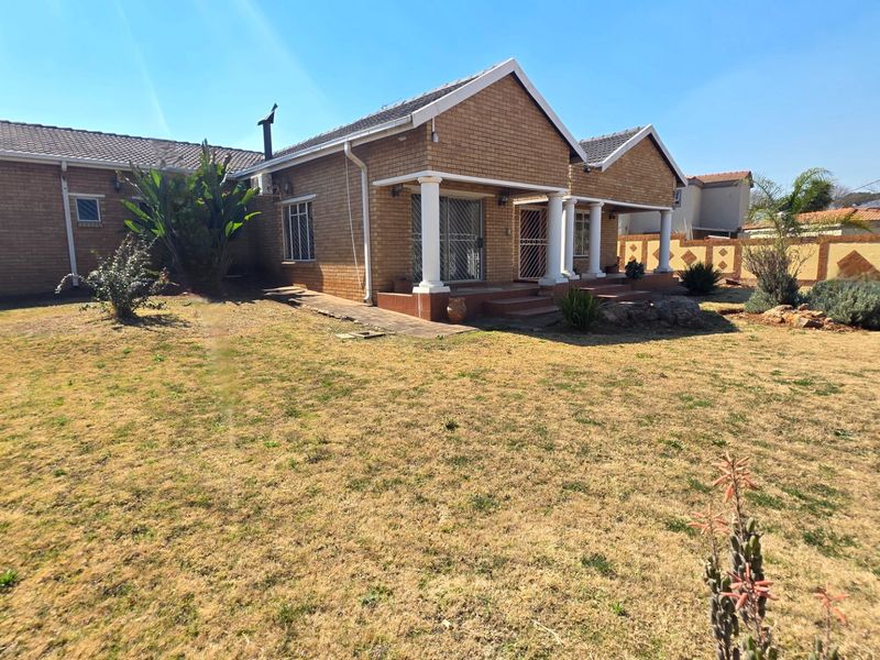 Rear view of a single-story brick house featuring a covered patio with decorative columns and a large surrounding garden area.