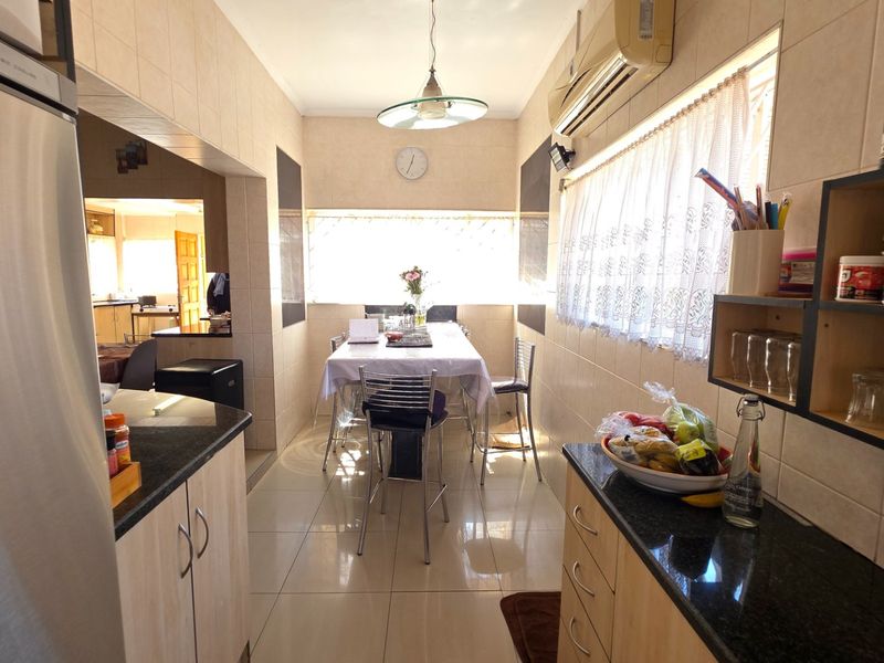A functional kitchen featuring granite countertops, tiled walls and flooring, and a wall-mounted air conditioning unit, with an integrated dining area.