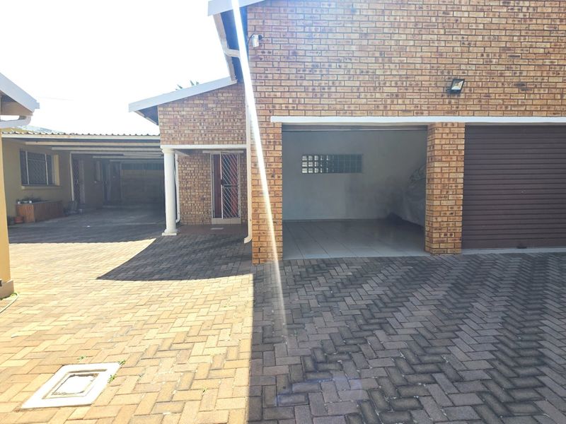Exterior view of a brick house featuring a paved driveway, a garage with a roller door, and a covered entrance area.