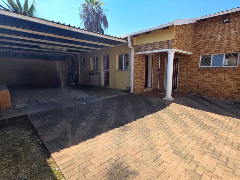 Front exterior view of the property featuring a brick facade, paved driveway, and a covered carport area.
