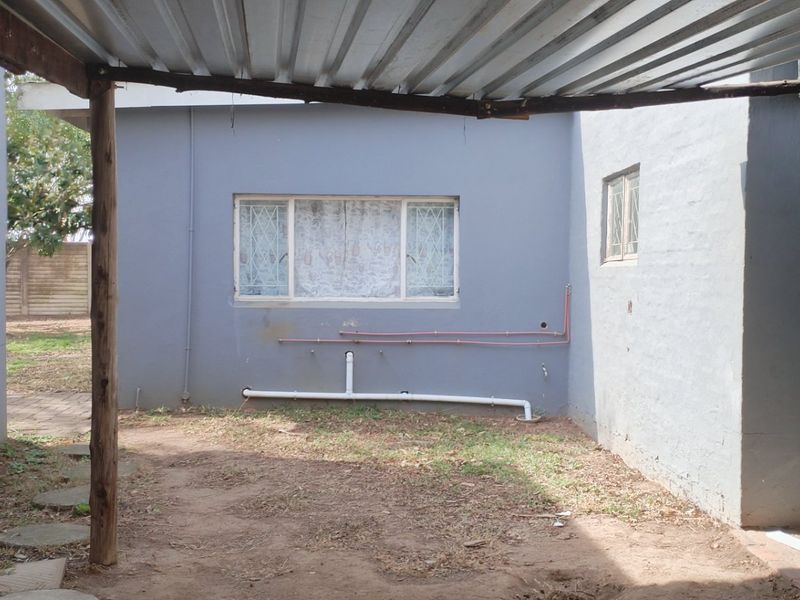 Rear exterior view showing a covered area with corrugated metal roofing, exposed plumbing, and a roller shutter door.