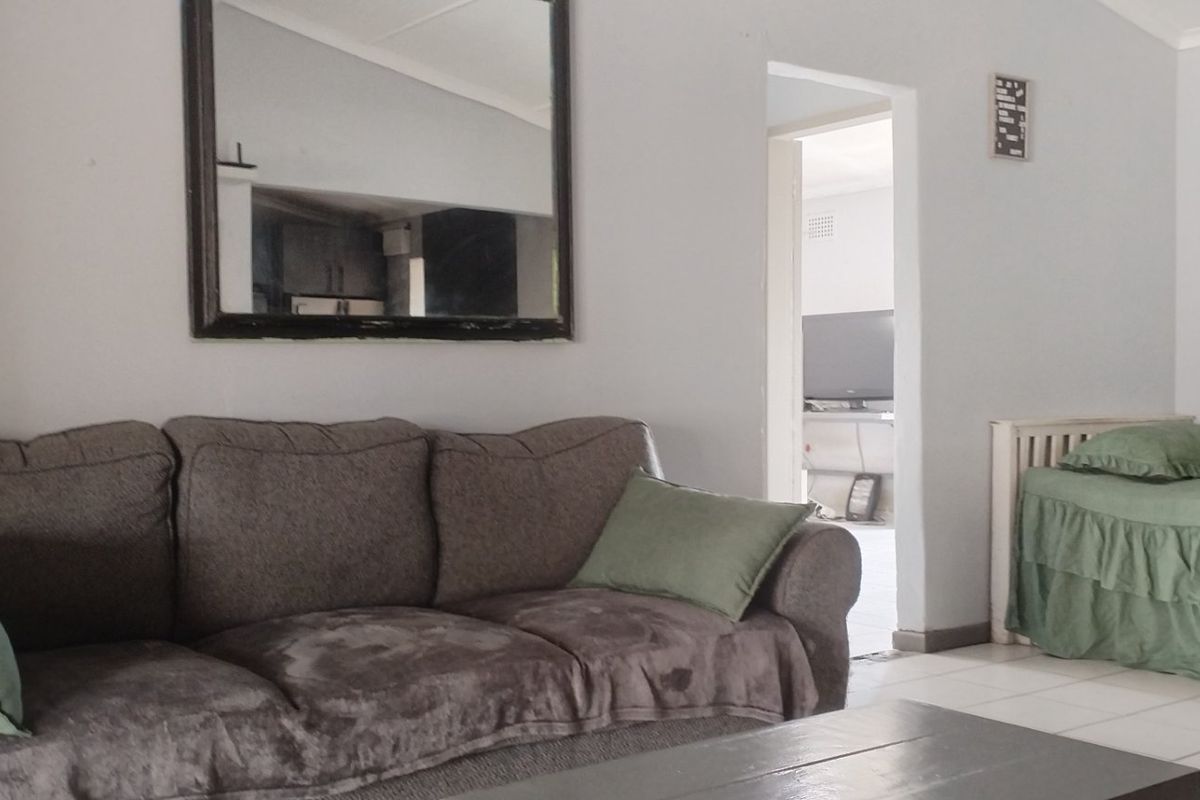 A living room area featuring tiled flooring and coved ceilings, with an open doorway leading to an adjacent room.