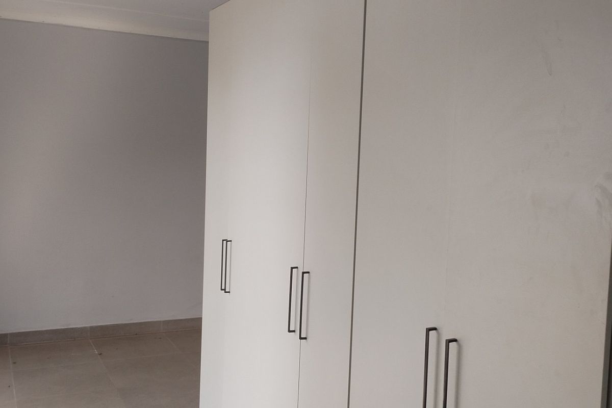 A clean, empty bedroom featuring modern built-in cupboards with sleek handles and neutral tiled flooring.