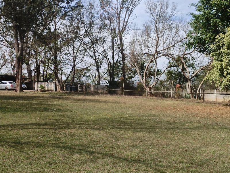 A spacious, open garden area featuring established trees and perimeter fencing, offering a large outdoor space.