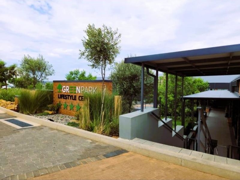 Exterior view of the Greenpark Lifestyle Centre featuring a paved entrance, modern metal canopy, and landscaped brick signage wall.