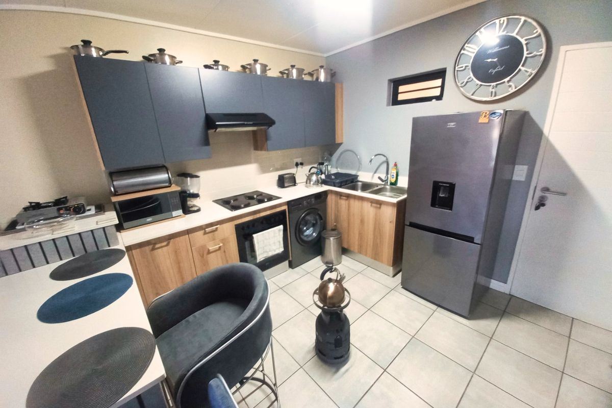 A functional kitchen featuring modern two-tone cabinetry, laminate countertops, built-in oven and hob, and tiled flooring with an integrated washing machine.