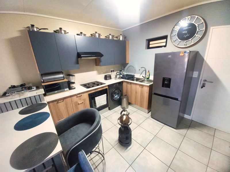 A functional kitchen featuring modern two-tone cabinetry, laminate countertops, built-in oven and hob, and tiled flooring with an integrated washing machine.