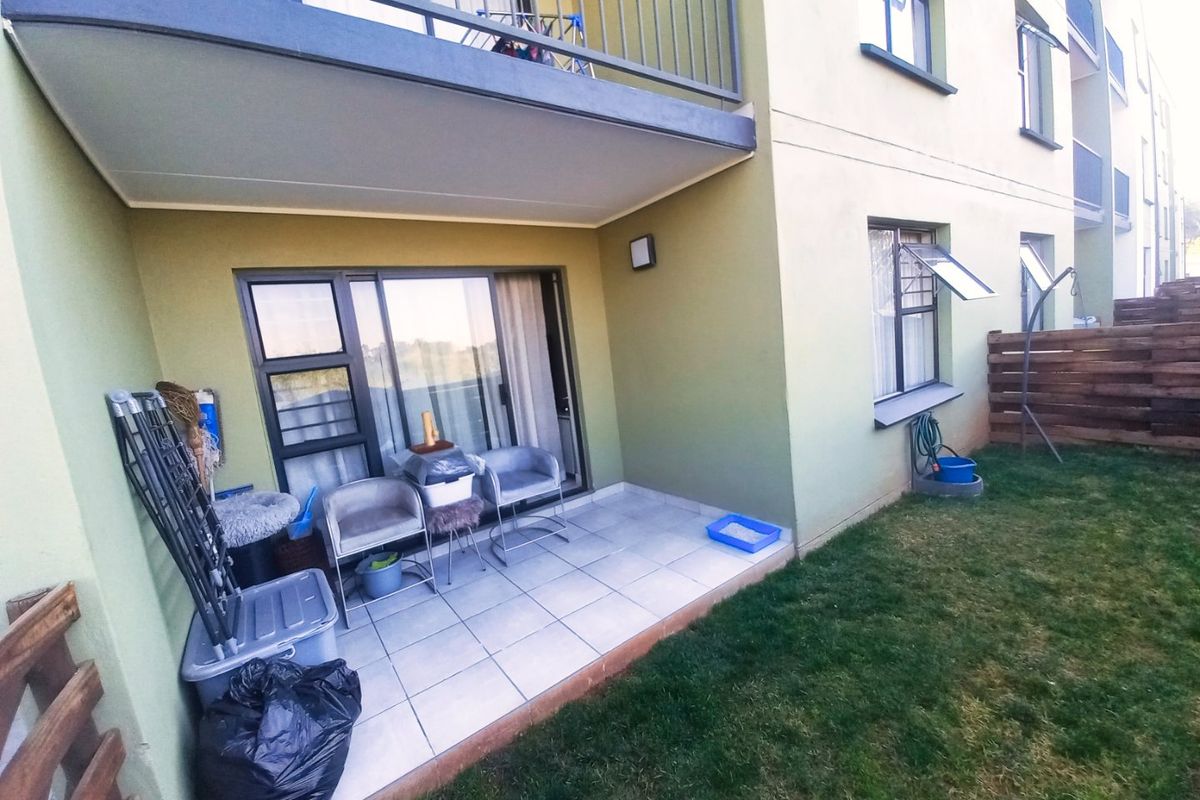 Ground floor apartment featuring a tiled patio area with sliding door access, overlooking a small private lawn and upper-level balcony.