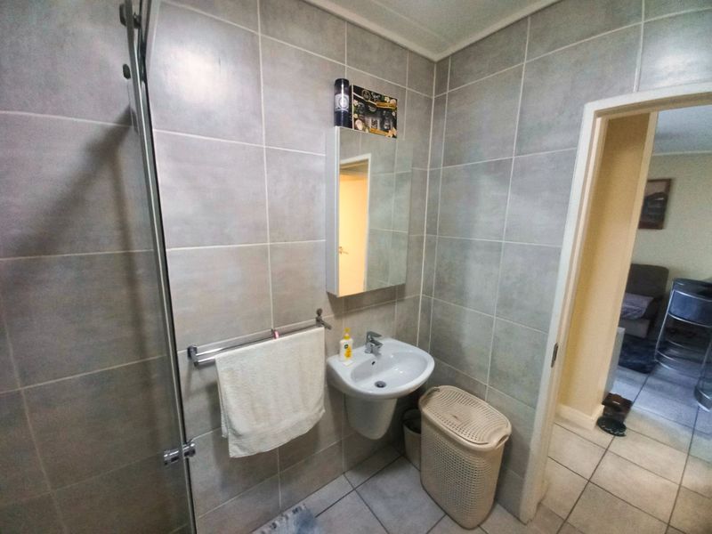 A functional bathroom featuring grey wall tiles, a wall-mounted basin with a chrome mixer tap, and a mirrored medicine cabinet.