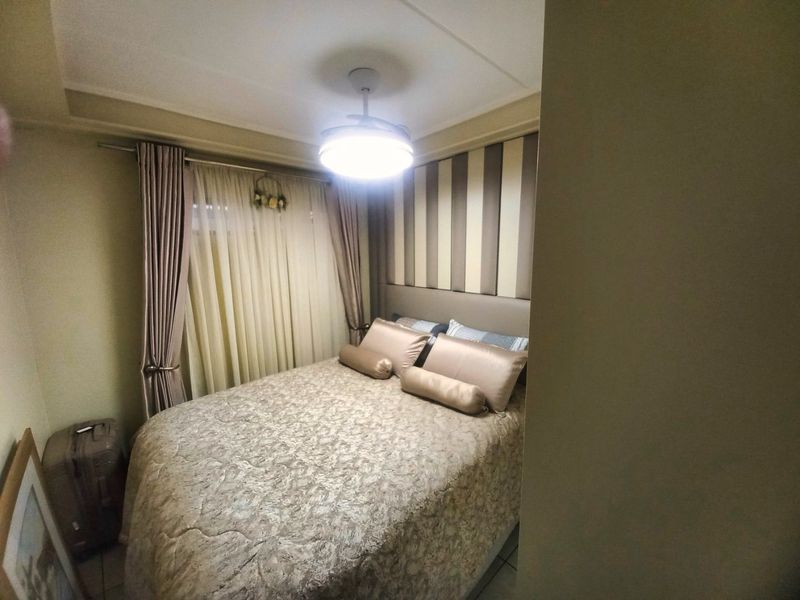 A compact bedroom featuring a built-in upholstered headboard, ceiling fan, and curtain rails, providing a functional sleeping space.