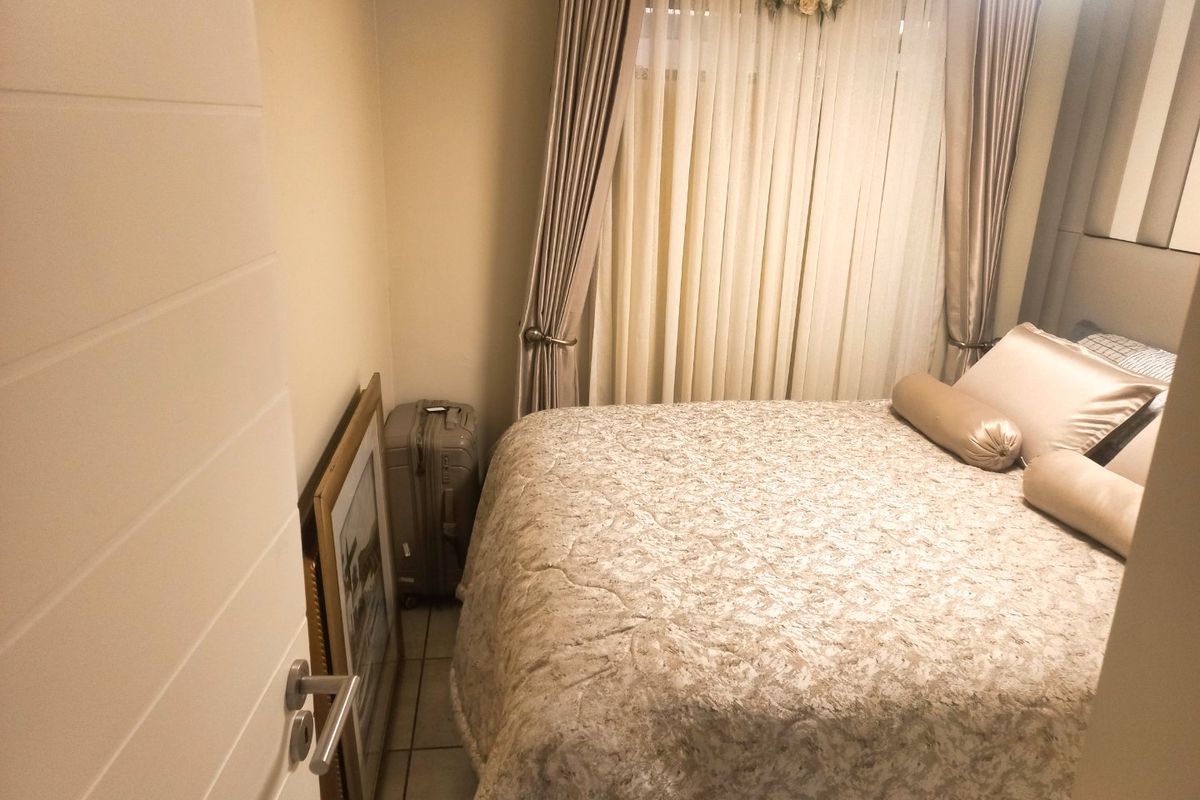 A compact bedroom featuring tiled flooring and neutral wall finishes, providing a functional sleeping space with natural light through window curtains.