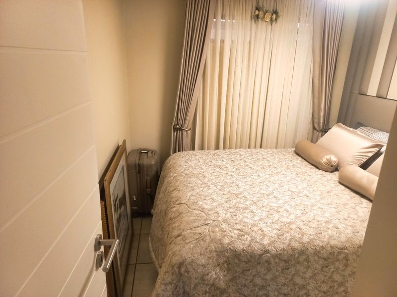 A compact bedroom featuring tiled flooring and neutral wall finishes, providing a functional sleeping space with natural light through window curtains.