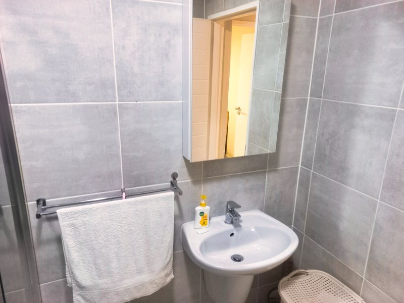 A clean bathroom featuring a wall-mounted basin with a chrome mixer tap, a mirrored medicine cabinet, and neutral grey ceramic wall tiling.