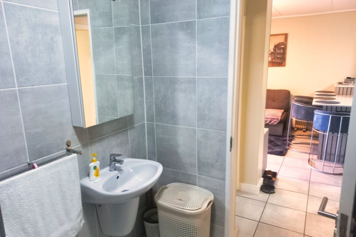A compact bathroom featuring grey wall tiles, a wall-mounted basin with a mixer tap, and a mirrored medicine cabinet.