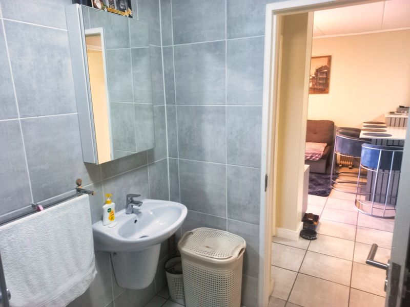 A compact bathroom featuring grey wall tiles, a wall-mounted basin with a mixer tap, and a mirrored medicine cabinet.