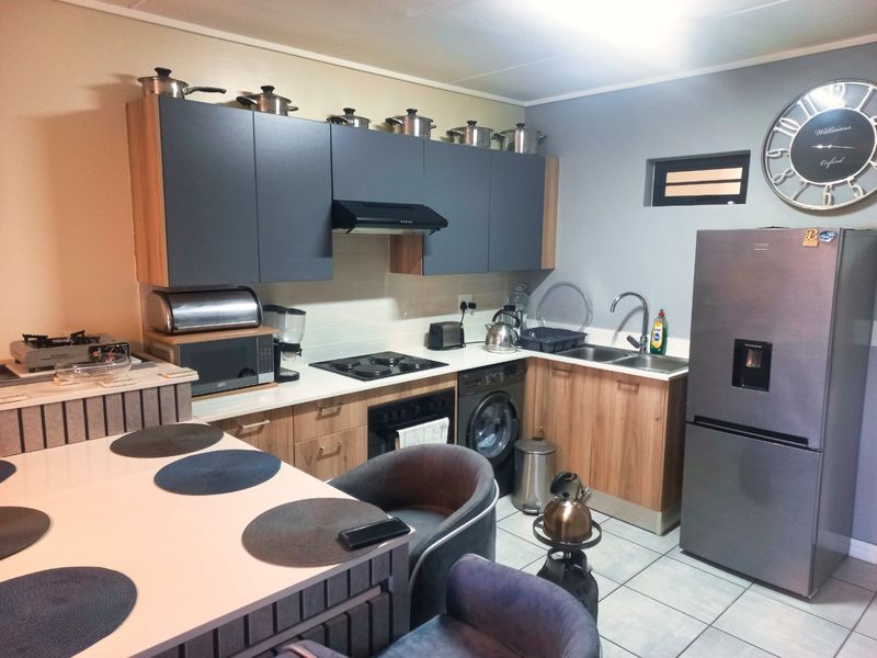 A functional kitchen featuring modern two-tone cabinetry, built-in appliances including an oven and hob, integrated washing machine, and tiled flooring.