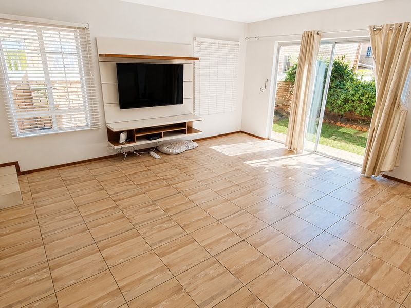 Spacious living room featuring tiled flooring, a built-in media console, and large sliding glass doors providing direct access to the rear garden.