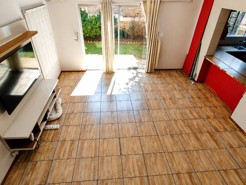 Open-plan living area featuring tiled flooring, a sliding door to the garden, and a convenient pass-through window connecting to the kitchen.