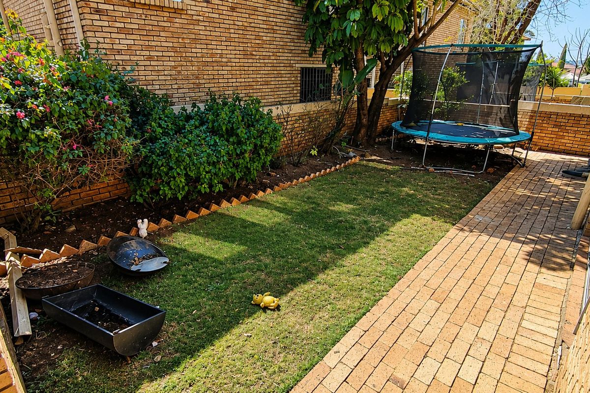 A private rear garden area featuring a brick boundary wall, a paved walkway, and a small lawn space.