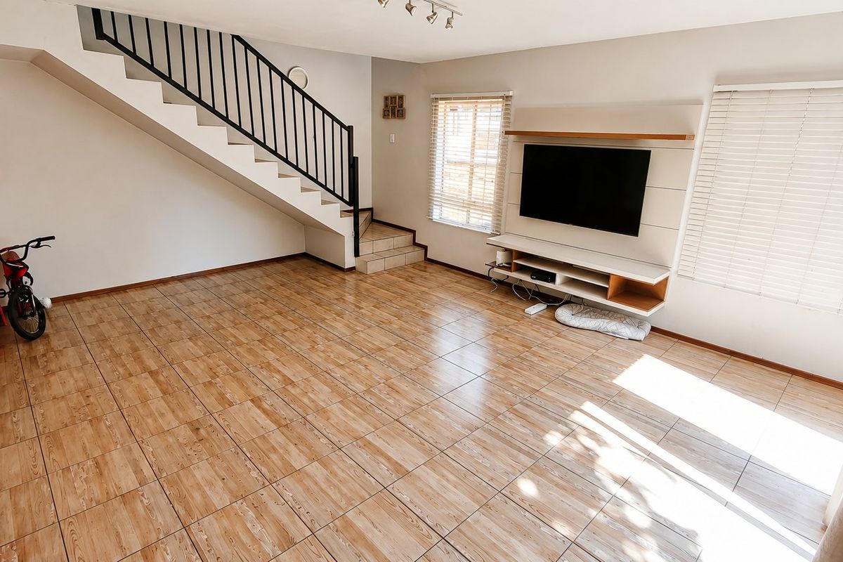 Spacious living room featuring tiled flooring, a built-in media unit, and a staircase with a metal balustrade.