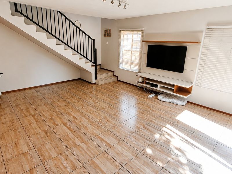 Spacious living room featuring tiled flooring, a built-in media unit, and a staircase with a metal balustrade.